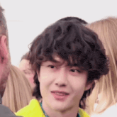 a young man with curly hair is wearing a yellow shirt and smiling