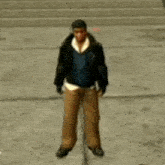 a man in a black jacket and brown pants is standing on a sidewalk in a video game .