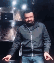 a man with a beard is dancing in a dark room while wearing a black jacket .