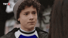 a young boy with curly hair is wearing a beanie and a blue shirt with trt1 written on the bottom