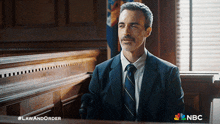 a man in a suit and tie sits in a courtroom with a nbc logo in the background