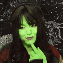 a woman with green face paint is wearing headphones and looking at her phone .