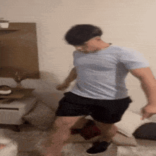 a man in a blue shirt and black shorts is jumping on a couch in a living room .