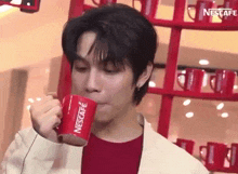a young man is drinking from a red nescafe cup .