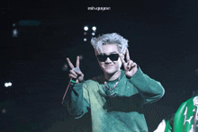 a man wearing sunglasses and a green shirt giving the peace sign