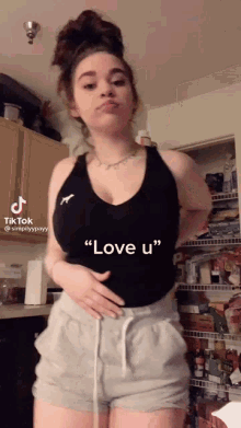 a woman in a black tank top and grey shorts says " love u " on a tiktok video