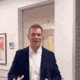 a man in a suit and white shirt is standing in front of a glass door and smiling .