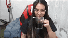 a woman wearing headphones and glasses is drinking a glass of cola .