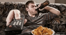a man sitting on a couch drinking a bottle of beer and holding a remote control