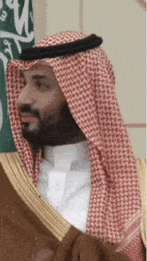 a man with a beard wearing a red and white head scarf stands in front of a green and white flag