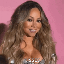mariah carey is smiling and giving a kiss to the camera while wearing a plunging neckline .