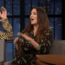 a woman in a floral dress is sitting in a chair with her hands in the air