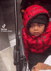 a little boy in a red jacket and black hat is sitting in a stroller