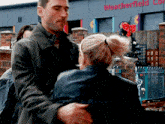 a man is hugging a woman in front of a weatherfield building