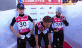 three athletes wearing orlen vests stand in front of a banner that says grand prix