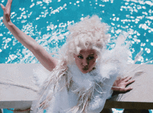 a woman in a white feathered outfit stands on a balcony