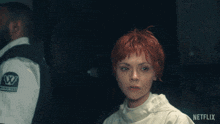 a woman with red hair is standing in front of a man with a w on his shirt