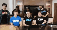 a group of young men wearing sdmn shirts are sitting around a table