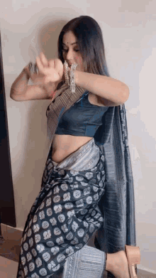 a woman in a blue crop top and a black and silver saree is dancing