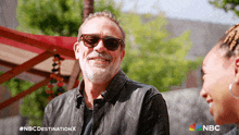 a man wearing sunglasses and a leather jacket is smiling while talking to a woman