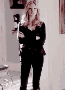 a woman in a black jacket and black pants is standing in a hallway with her arms crossed