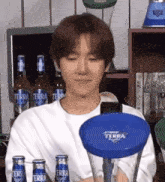 a young man in a white shirt is holding a blue terra light beer bottle .