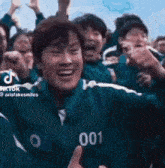 a group of people are playing a game called squid game and one of them is wearing a number 001 jacket .