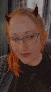 a woman wearing horns and glasses is sticking out her tongue