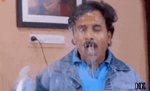 a man in a denim jacket is drinking water from a bottle with his mouth open .