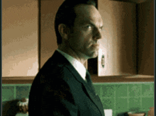 a man in a suit and tie is standing in a kitchen with green tiles