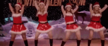 a group of women dressed as santa clauses are dancing on a stage .