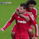 a man in a red bwin jersey is being lifted by another man on a soccer field .