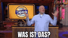 a man in a blue shirt is standing in front of a yellow sign that says ' was ist das ? ' on it .