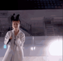 a woman in a white coat is singing into a microphone while wearing horns .