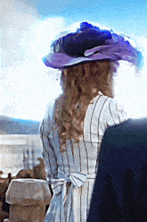 a woman wearing a striped dress and a purple hat stands in front of a blue sky