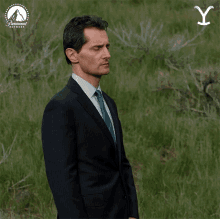 a man in a suit and tie stands in a field with a paramount network logo in the background