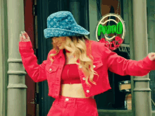 a woman wearing a denim hat and a red jacket is dancing in front of a sign that says ' uno '