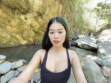 a woman in a black tank top is standing in front of a body of water