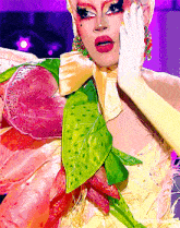 a drag queen is wearing a colorful costume with flowers and leaves .