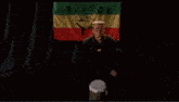 a man with a crown on his head is standing in front of a rastafari flag