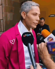 a man in a pink suit is being interviewed by someone with a microphone that says uotv on it