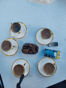 four cups of coffee on saucers next to a box of cigarettes and a lighter