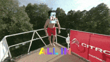 a man in red shorts is jumping off a diving board with the words all in below him