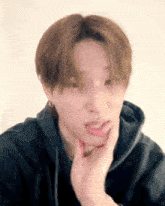 a young man wearing a black hoodie is making a funny face .