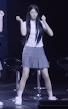 a girl in a white shirt and blue skirt is dancing on stage