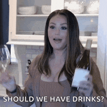 a woman is holding a bottle of wine and a glass and says should we have drinks .