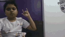 a young boy wearing a sailboat shirt is making a devil horns gesture