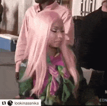 a woman with long pink hair is standing in front of a man in a pink shirt and scarf .