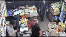 a man in a suit is standing in a store behind a counter while a man in a black shirt stands behind him