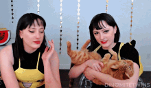 two women are holding a cat in their arms and the words dinomite twins are above them
